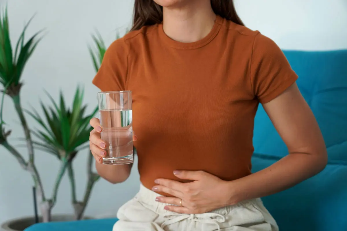 Woman holding a glass of water and touching her stomach, showing digestive discomfort