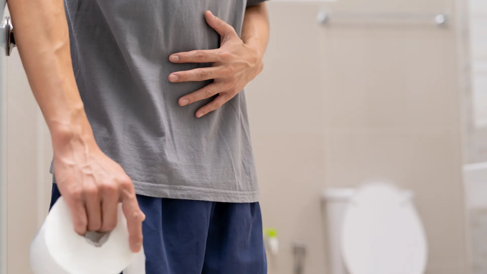 diarrhea picture blog 1 Man with stomach pain in a bathroom, holding toilet paper, showing diarrhea symptoms